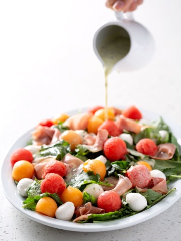 pouring dressing over platter of salad on white counter