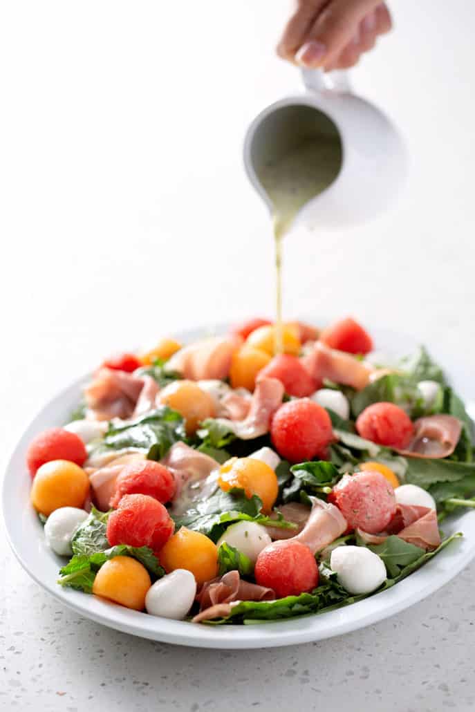 pouring dressing over salad on platter on white background