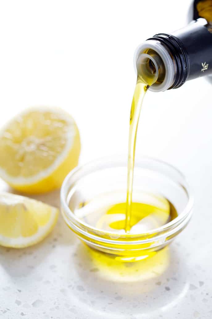 olive oil being poured into small bowl next to lemons