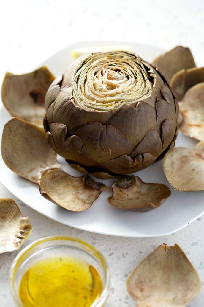 whole baked artichoke on plate with artichoke dipping sauce on the side