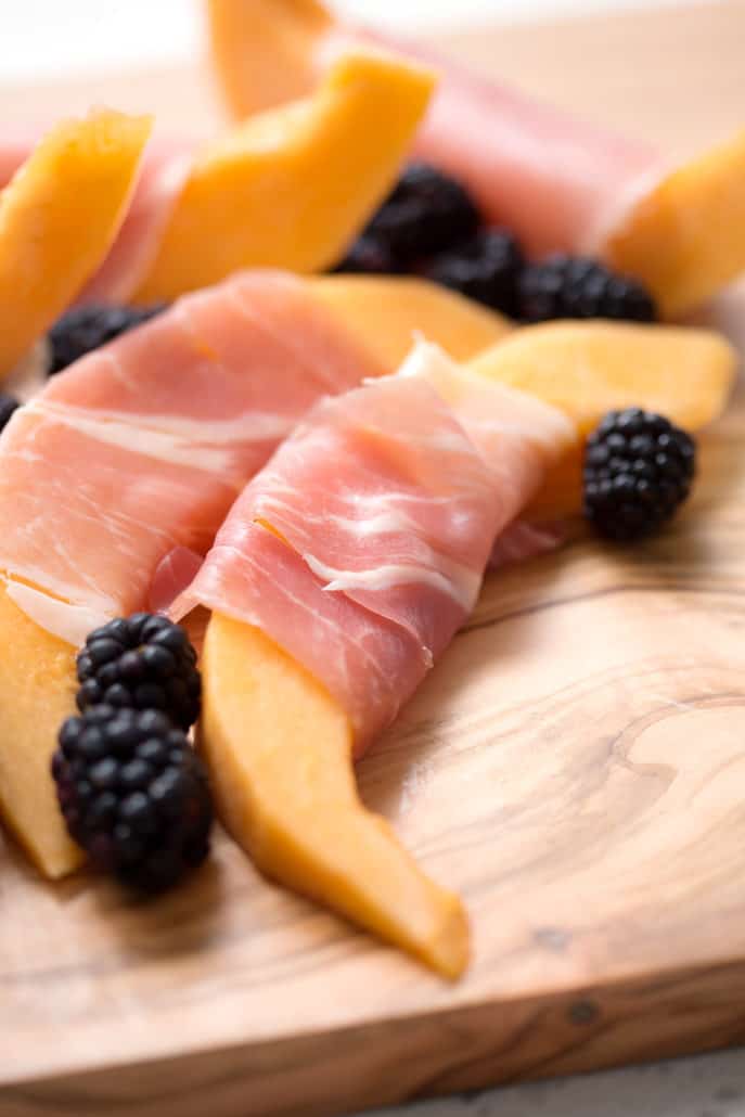 slices of cantaloupe wrapped in prosciutto on cutting board