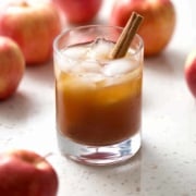 glass of kombucha with cinnamon stick surrounded by apples