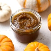 jar of pumpkin butter surrounded by pumpkins on white background