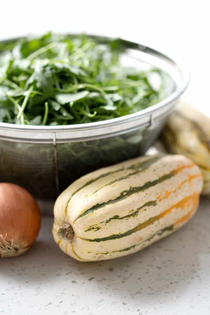 strainer filled with arugula and winter squash on white background