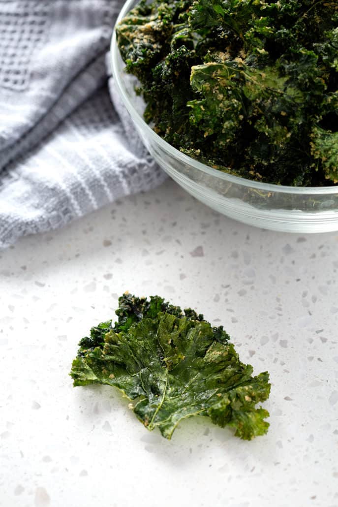 kale chip on counter in front of bowl of kale chips and towel