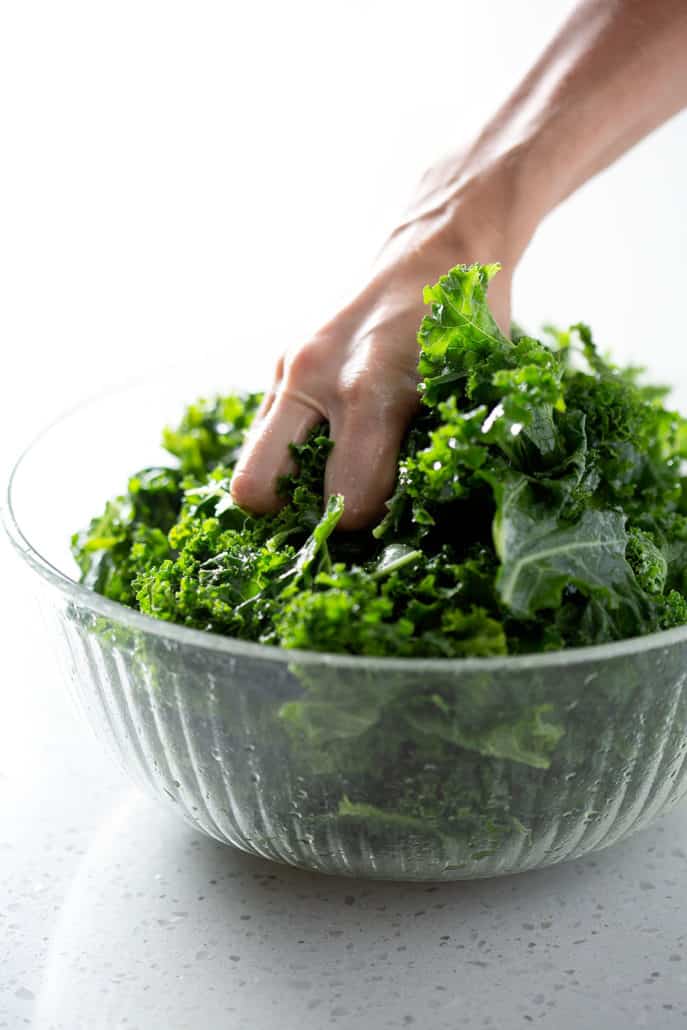 hand massaging kale in bowl