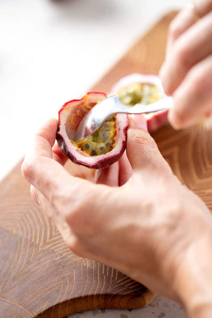 hands holding shell of passion fruit while scoping out insides with a spoon