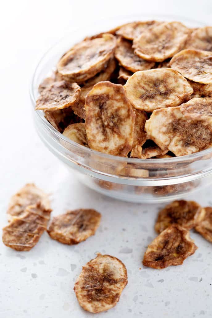 cinnamon dehydrated banana chips in bowl on white background