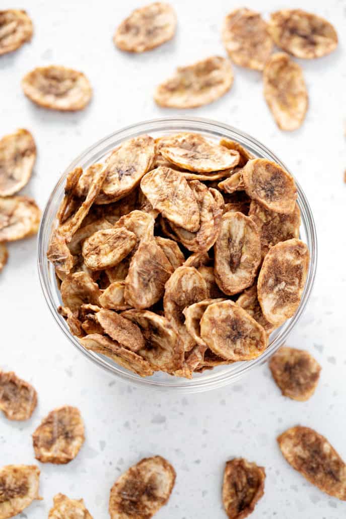 Bowl of dehydrated banana chips surrounded by banana chips from above