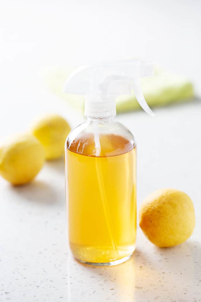 spray bottle with yellow liquid on white background with blurred lemons