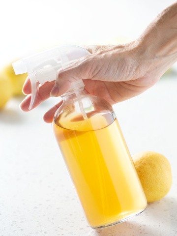 holding spray bottle of yellow liquid on white background