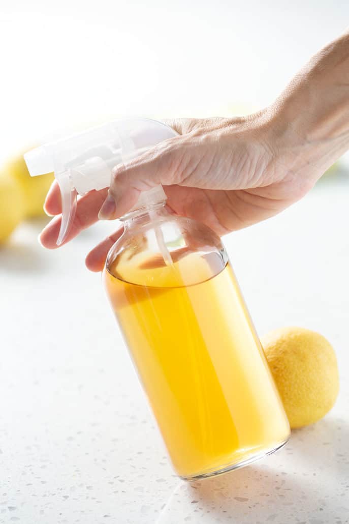 holding spray bottle of yellow liquid on white background