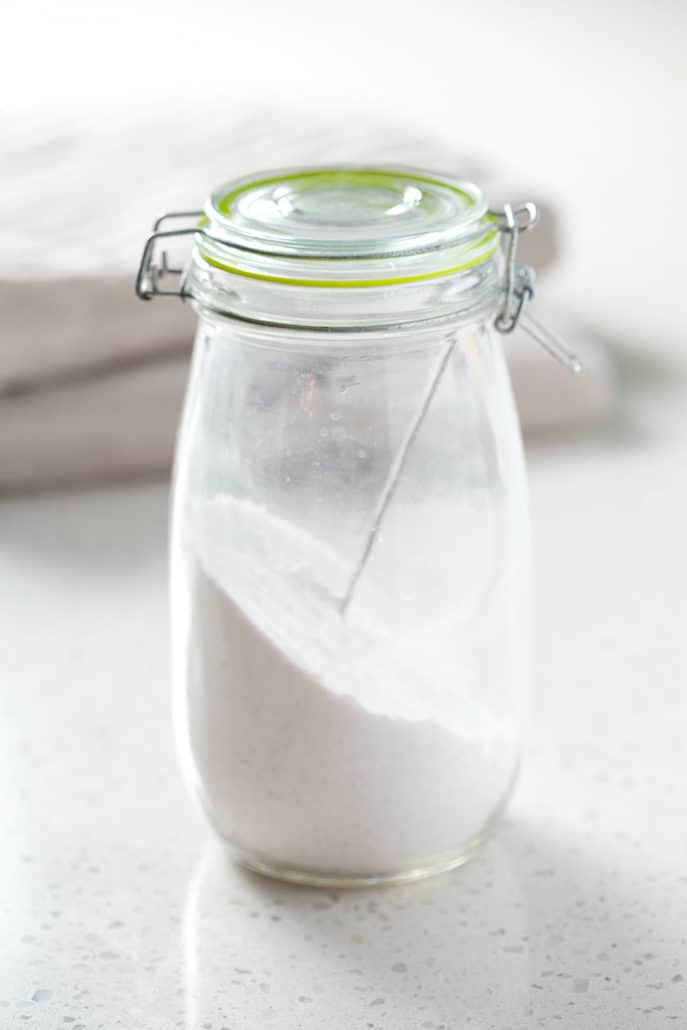 glass container of homemade laundry detergent powder with towels in background