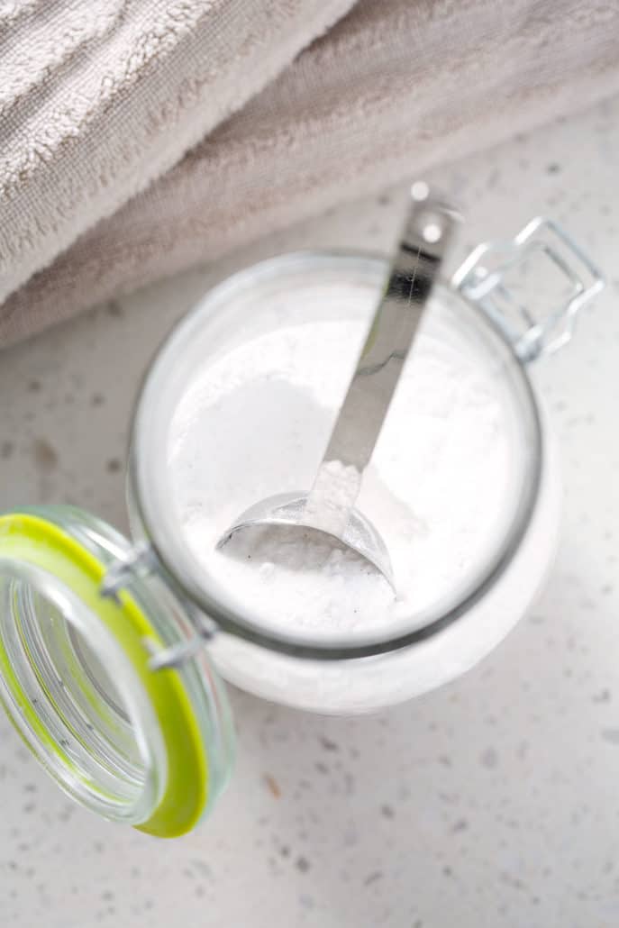container of homemade laundry detergent with spoon from above surrounded by towels