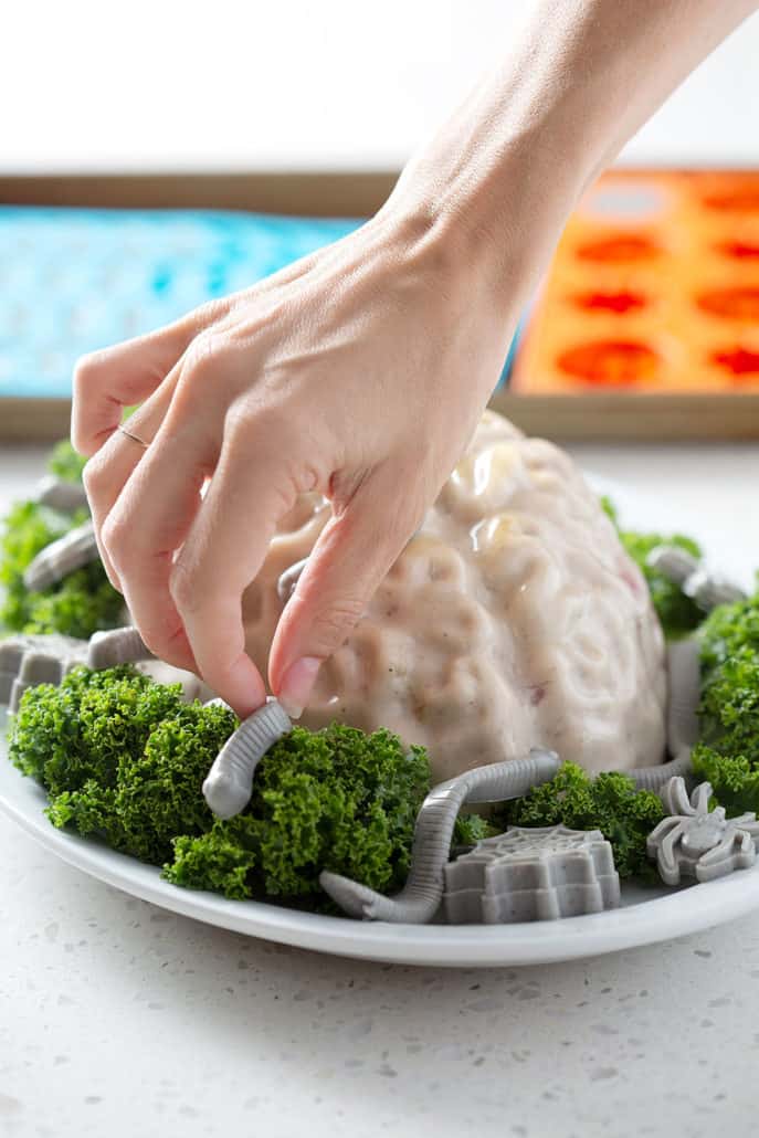 hand placing gummy worms on zombie brain dessert 