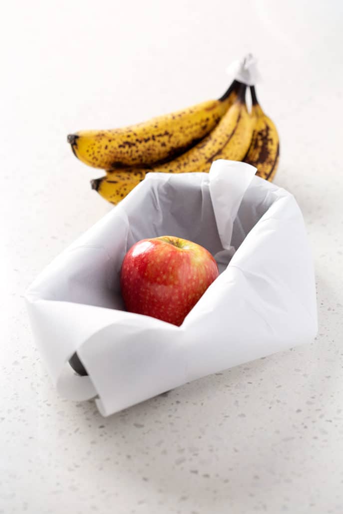 loaf pan lined with parchment paper with ripe banana and an apple