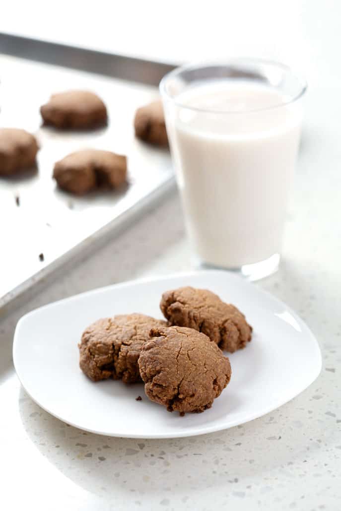 plate of cookies in front of glass of milk and baking sheet