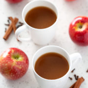 mugs of apple cider surrounded by apples and spices