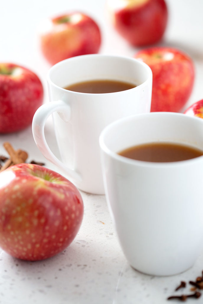 two mugs of apple cider surrounded by apples