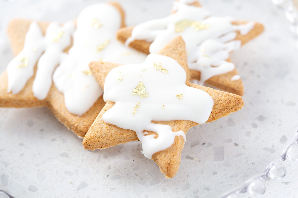 star cookies decorated with white frosting and gold flakes on glass plate