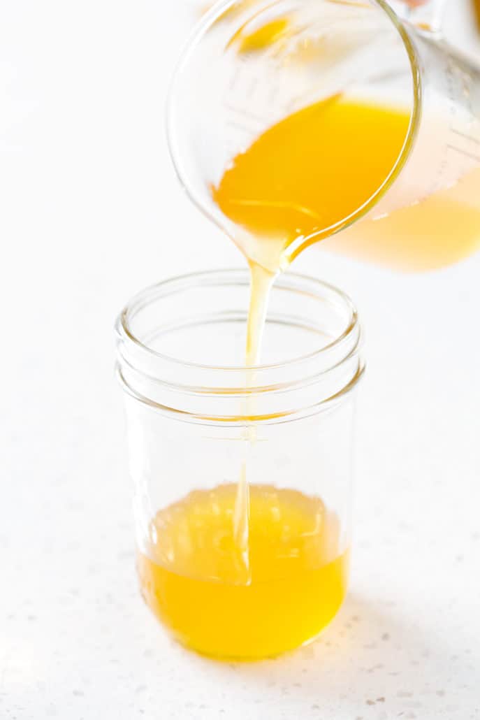 pouring ghee from measuring cup into mason jar