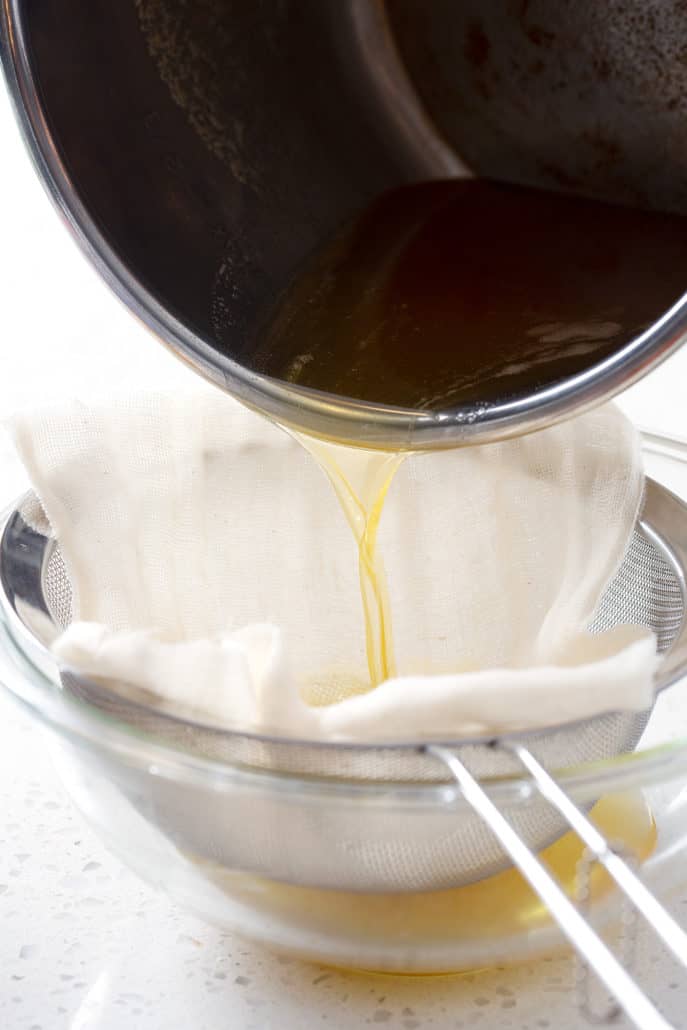 pouring ghee from instant pot into bowl over cheesecloth