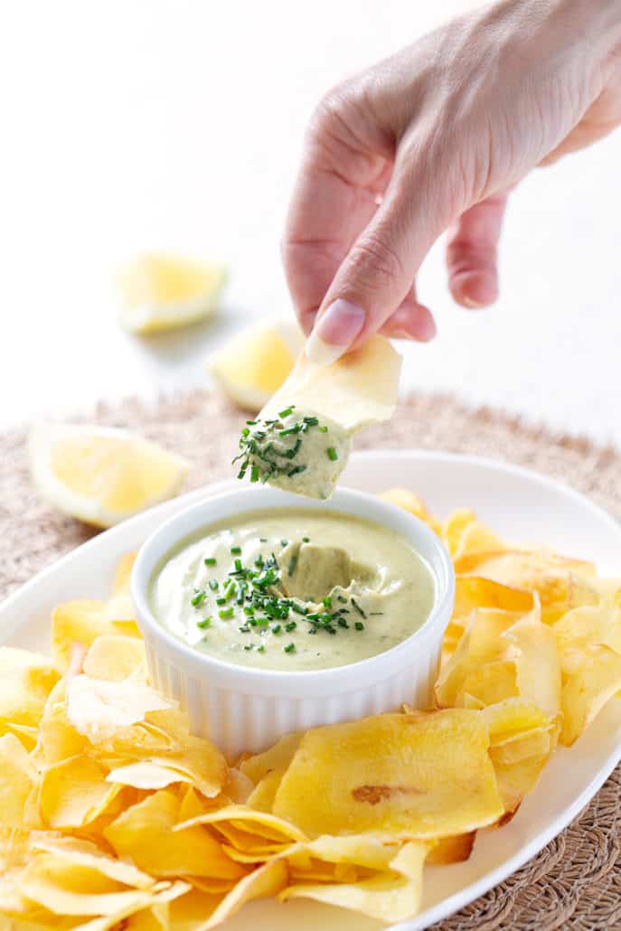 hand dipping chip into dip with chives