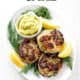 platter of aip salmon cakes surrounded by fresh dill, lemon slices and dip