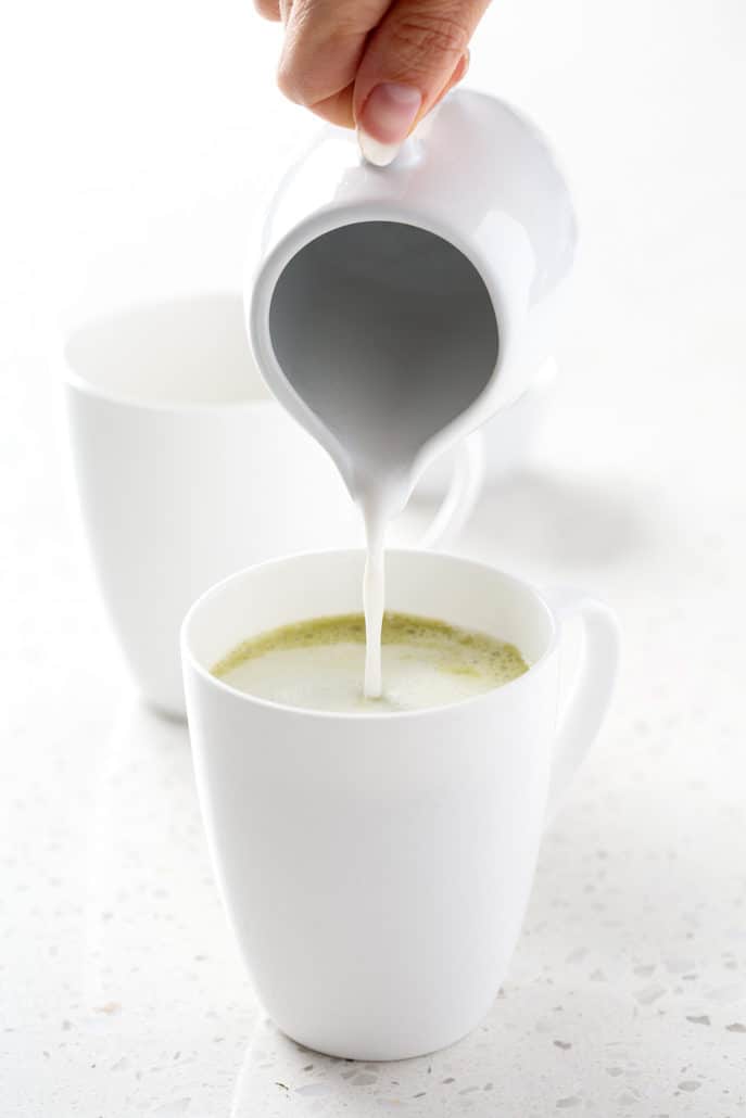pouring coconut milk into matcha tea on white background
