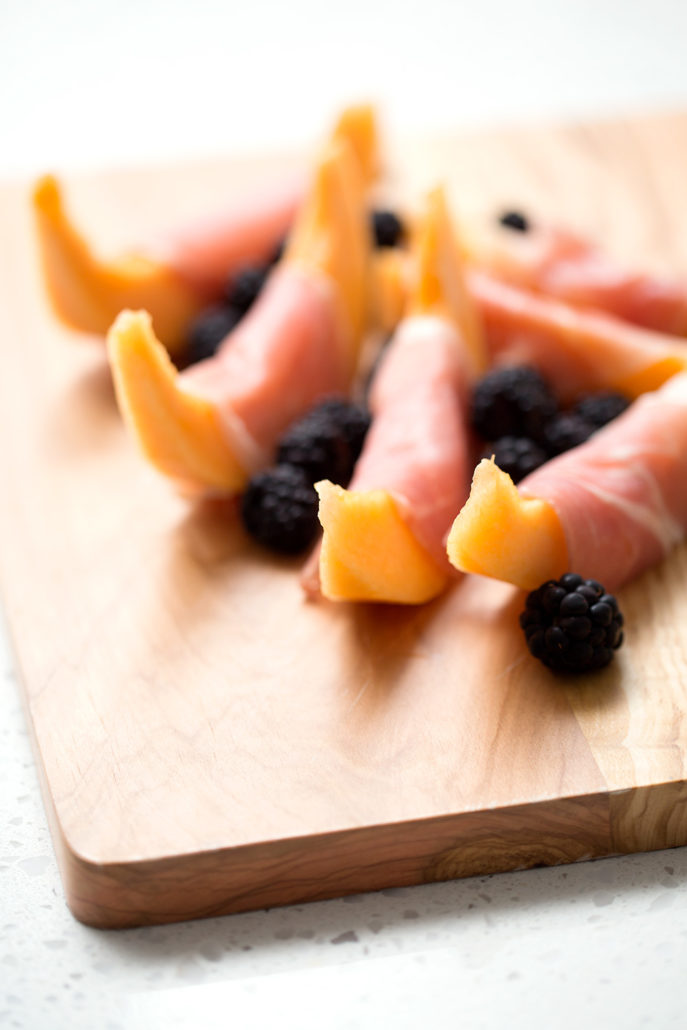 cantaloupe and prosciutto with blackberries on cutting board 