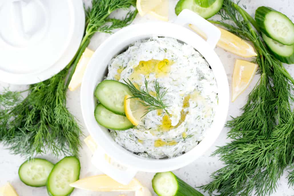 bowl of Dairy Free Tzatziki surrounded by dill, cucumbers and lemons