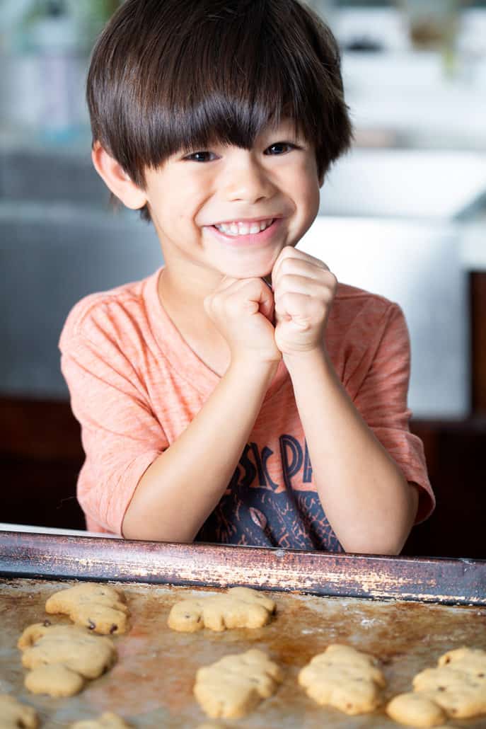 young boy smiling over baking sheet of AIP 'Chocolate' Chip Cut Out Cookies