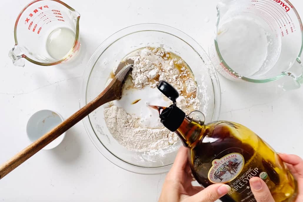 pouring maple syrup into mixing bowl surrounded by measuring cups and wooden spoon
