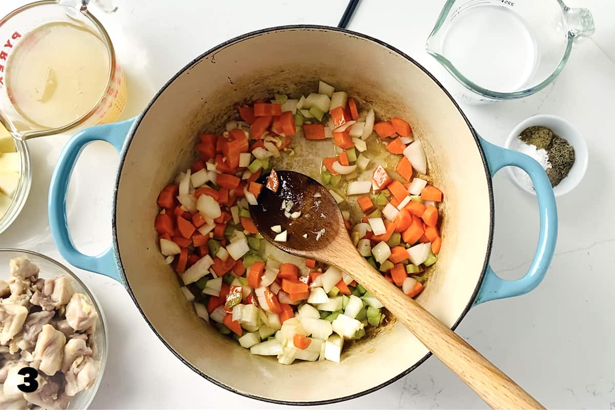 saute carrots, onions and celery in dutch oven surrounded by bowls of ingredients.