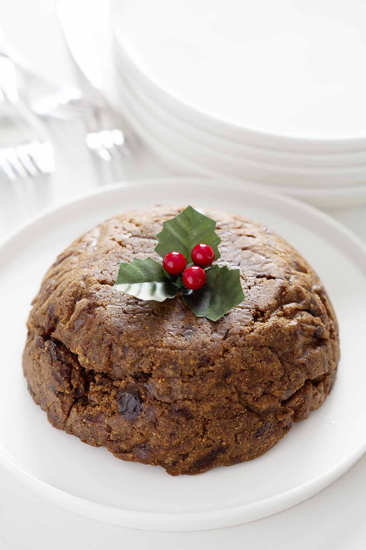 holly garnished Christmas pudding with flatware and plates in background
