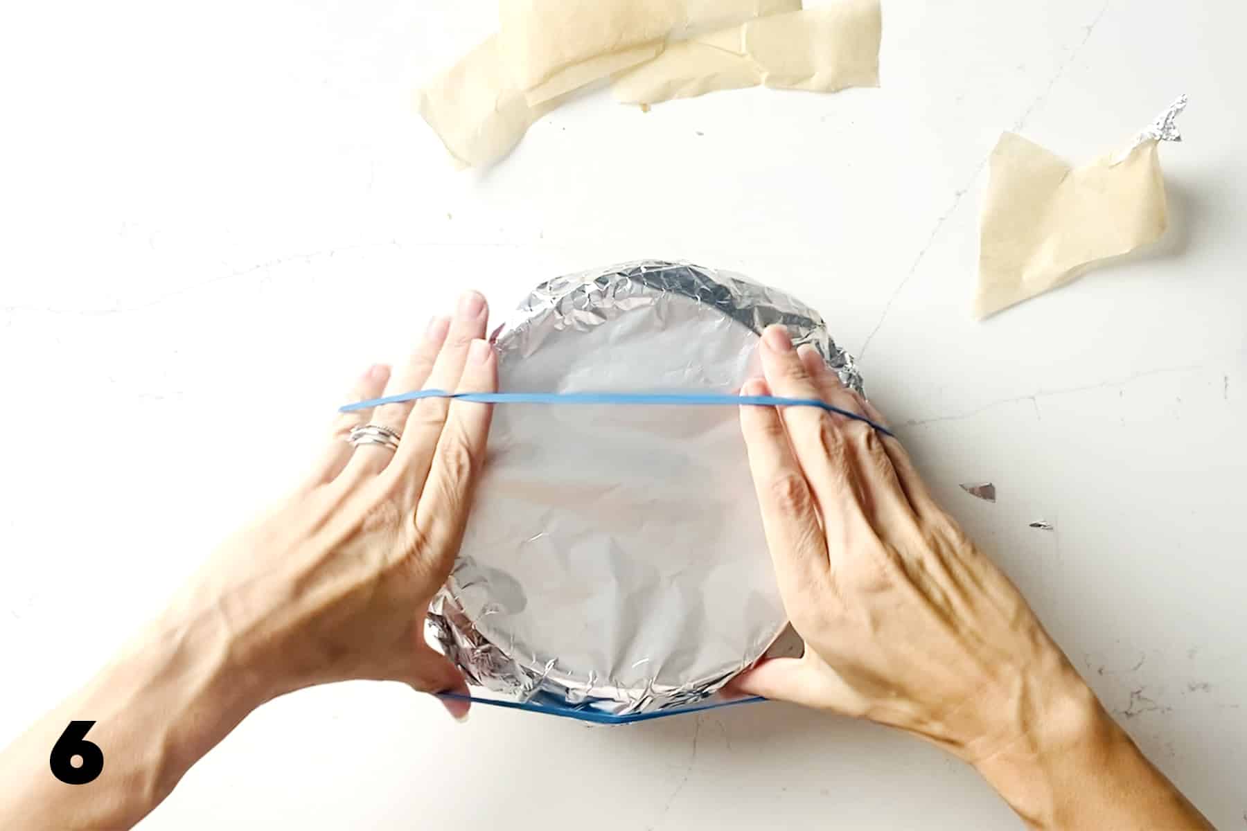 hands wrapping rubber band around top of foil covered bowl