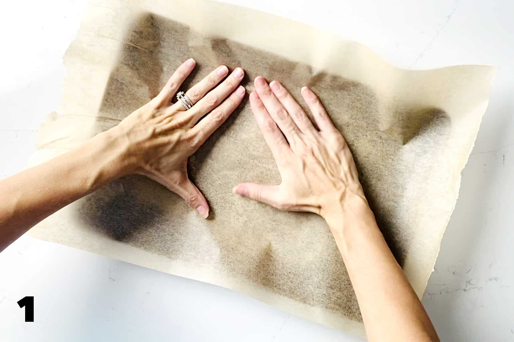 hands placing parchment paper on baking sheet