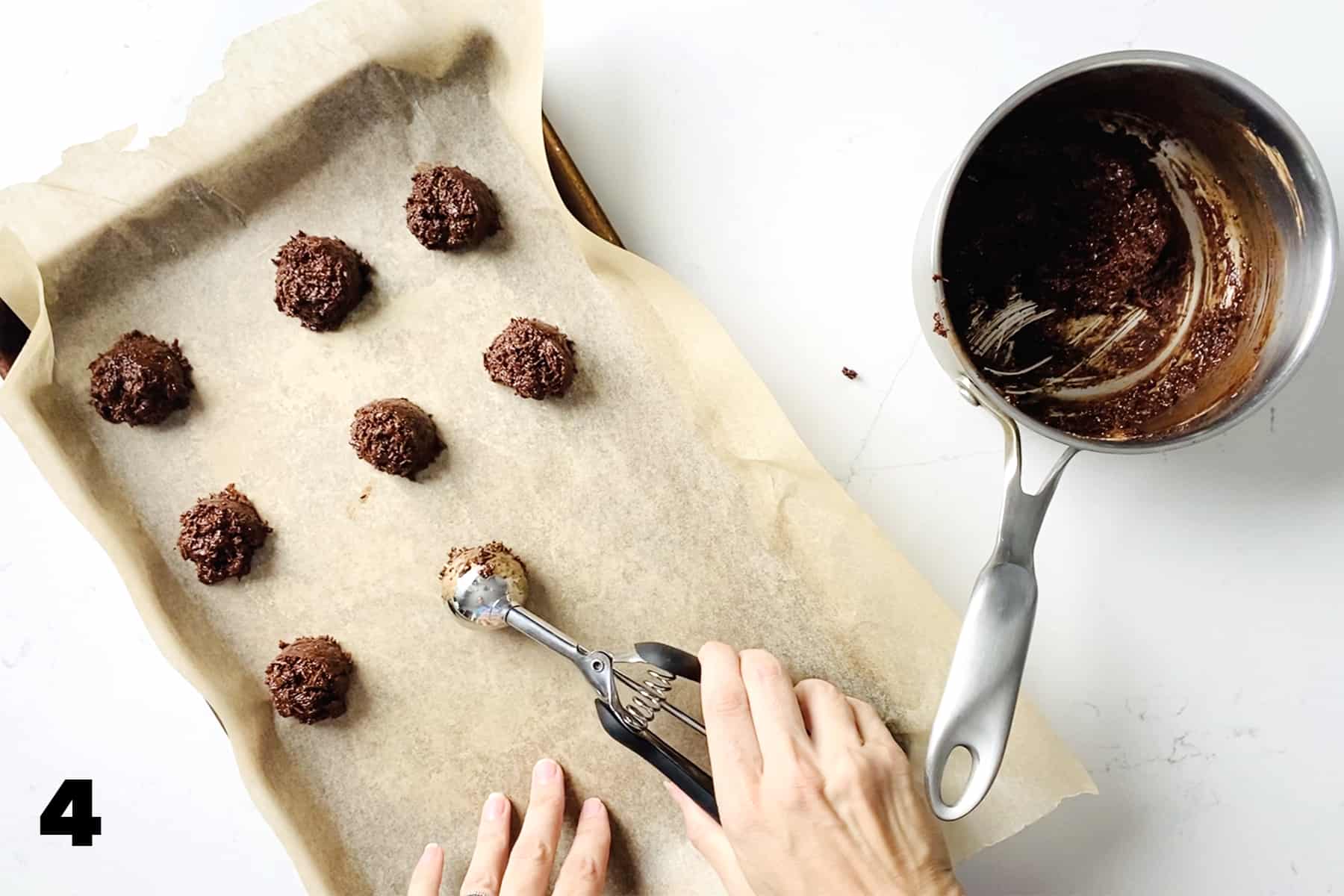 using scooper to scoop chocolate truffles into parchment lined baking sheet.
