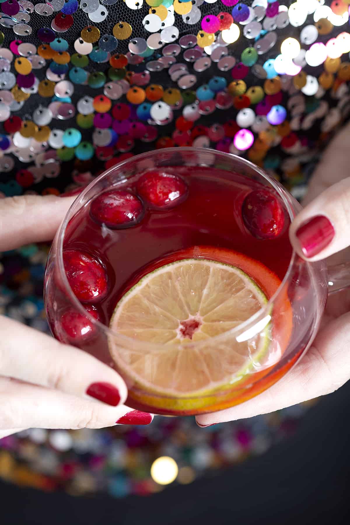 hands holding punch glass with citrus slices, red christmas punch and cranberries