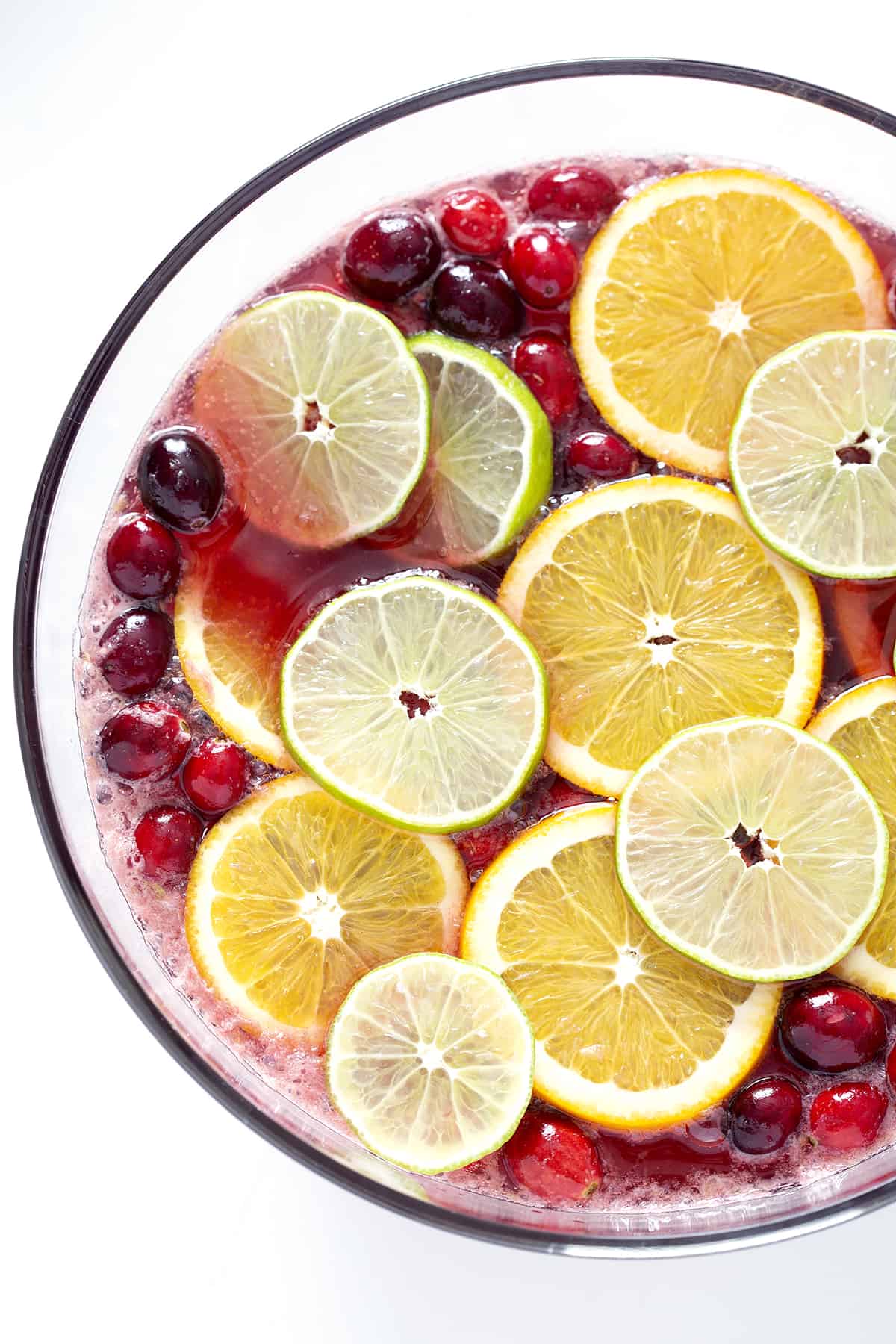 flat lay of punch bowl with slices of orange, lime and cranberries and juice
