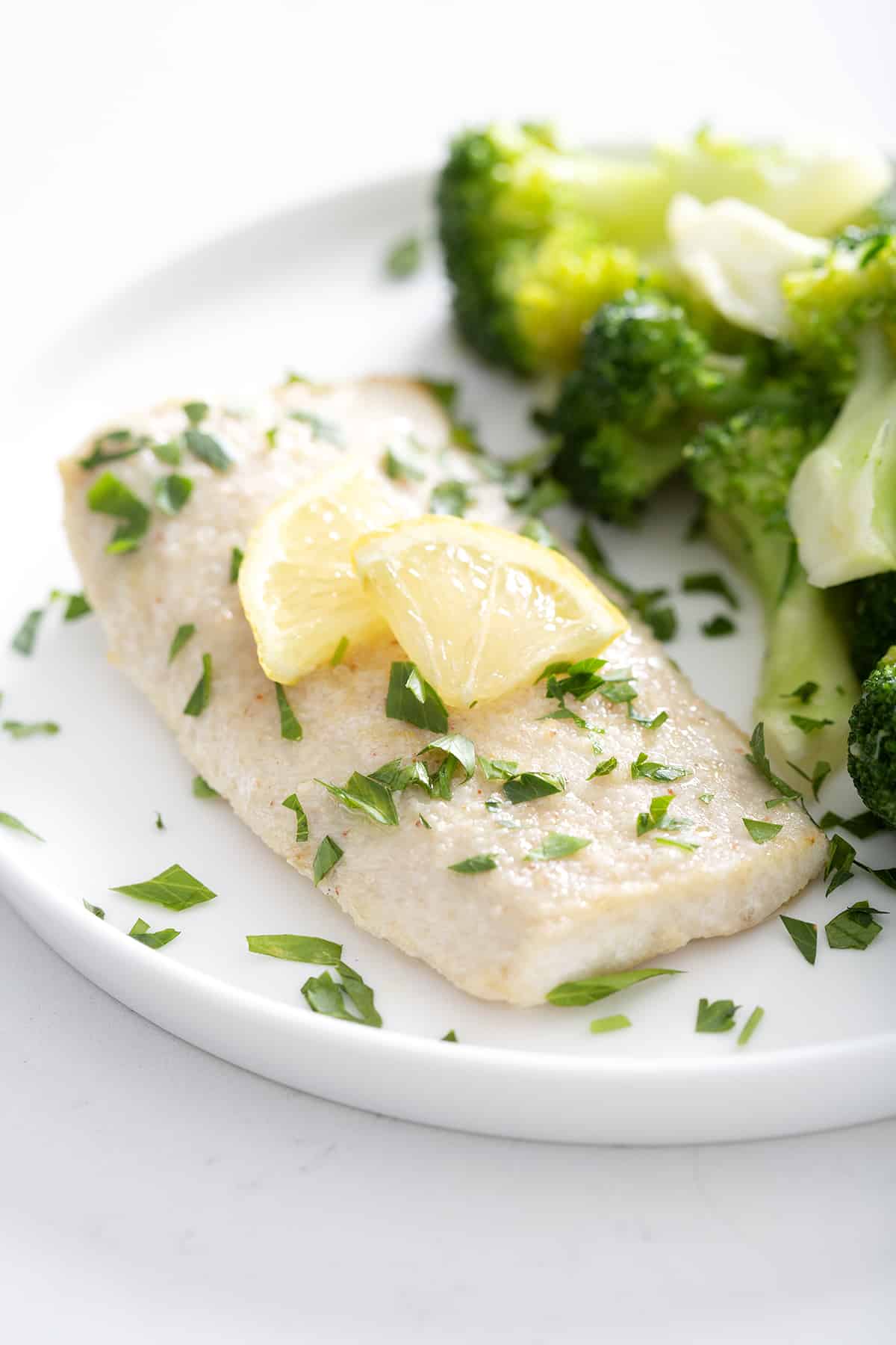 halibut fillet with parsley and lemon slices on plate with broccoli