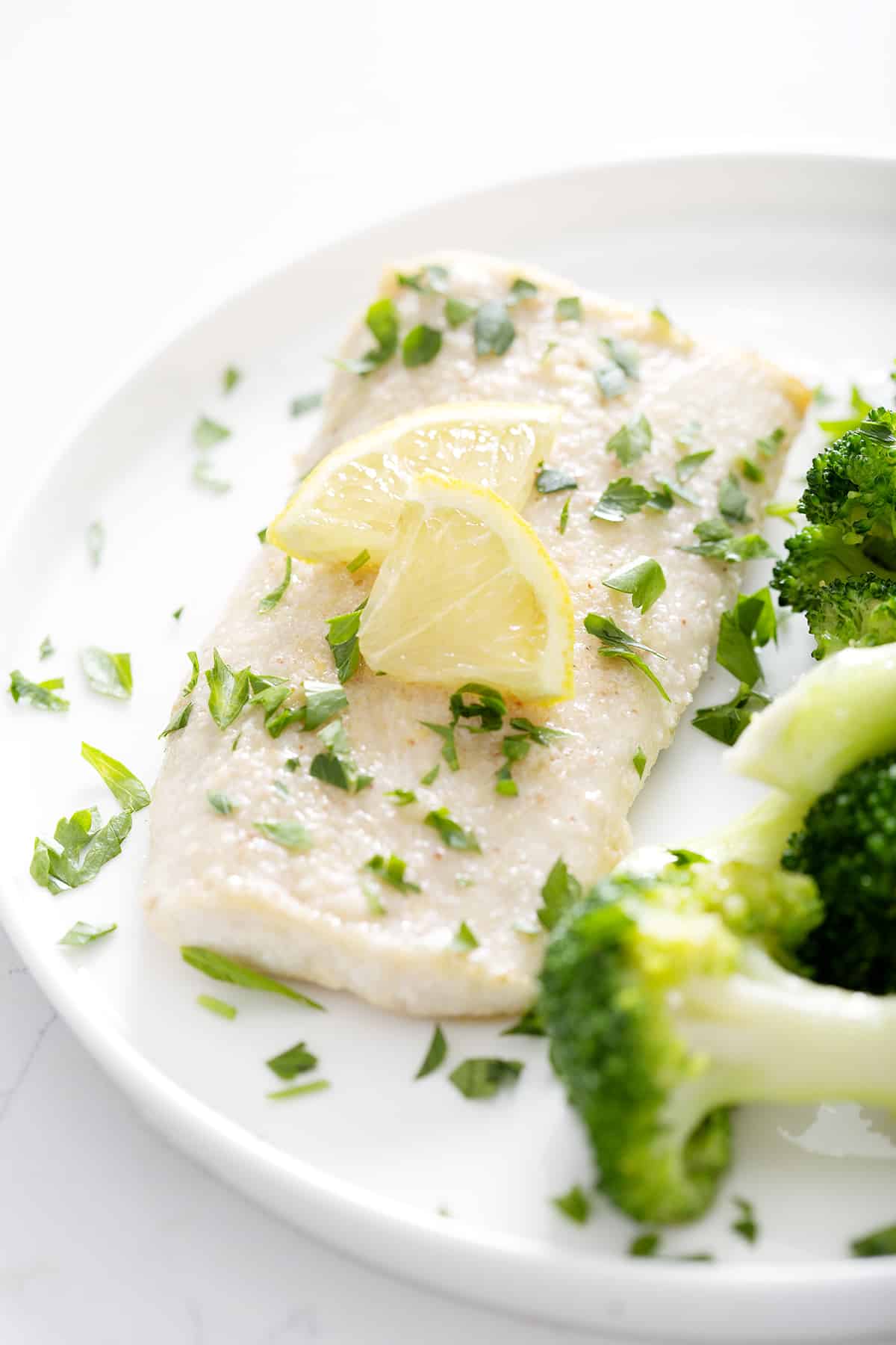 halibut fillet with parsley and lemon slices on white plate with broccoli