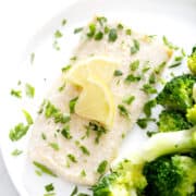 halibut fillet with parsley and lemon slices on plate with broccoli