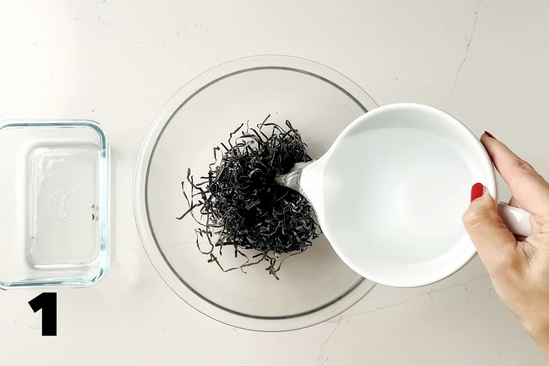 pouring water into glass bowl of dried seaweed