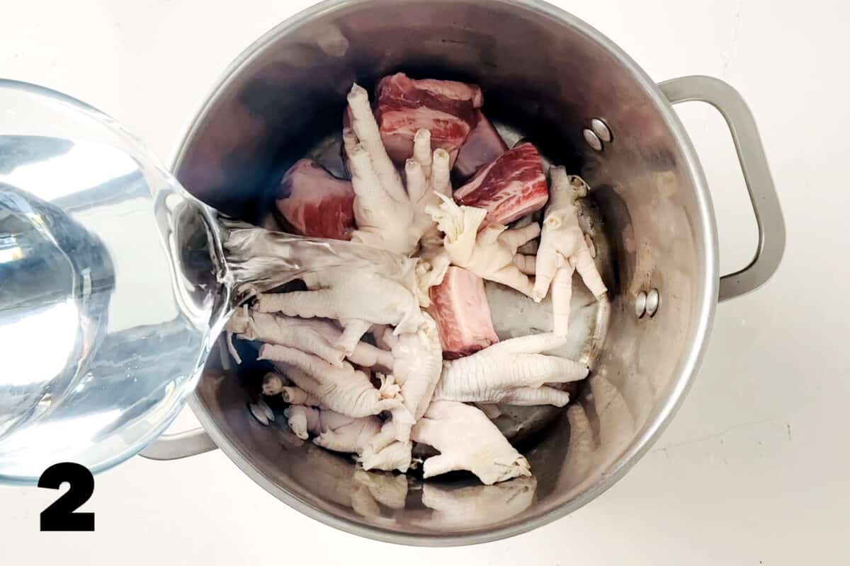 water being poured into stock pot of chicken feet and pork.