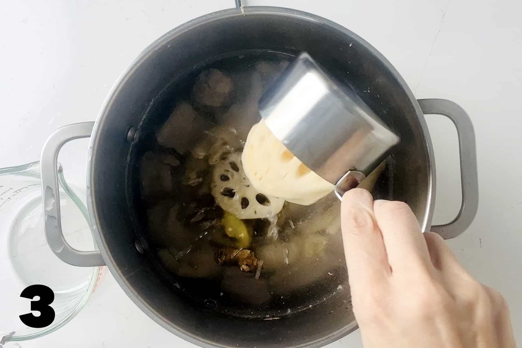 pouring sliced lotus root into stockpot with soup