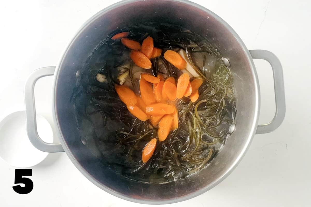 stock pot full of soup with sliced carrots on top.