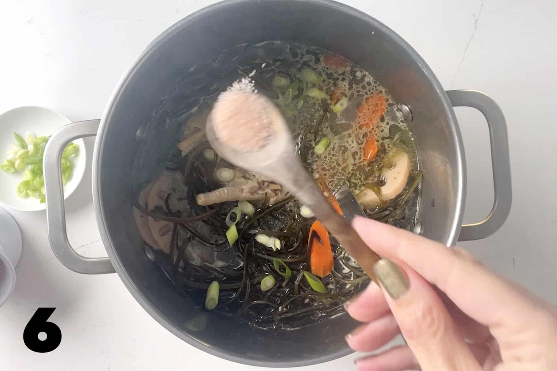 sprinkling salt into stock pot filled with chicken feet soup