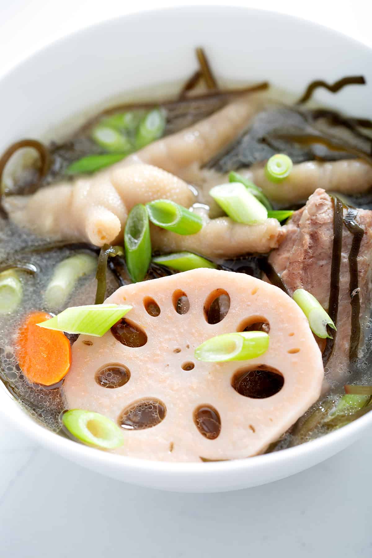 close up bowl of chicken feet soup with lotus root and green onions