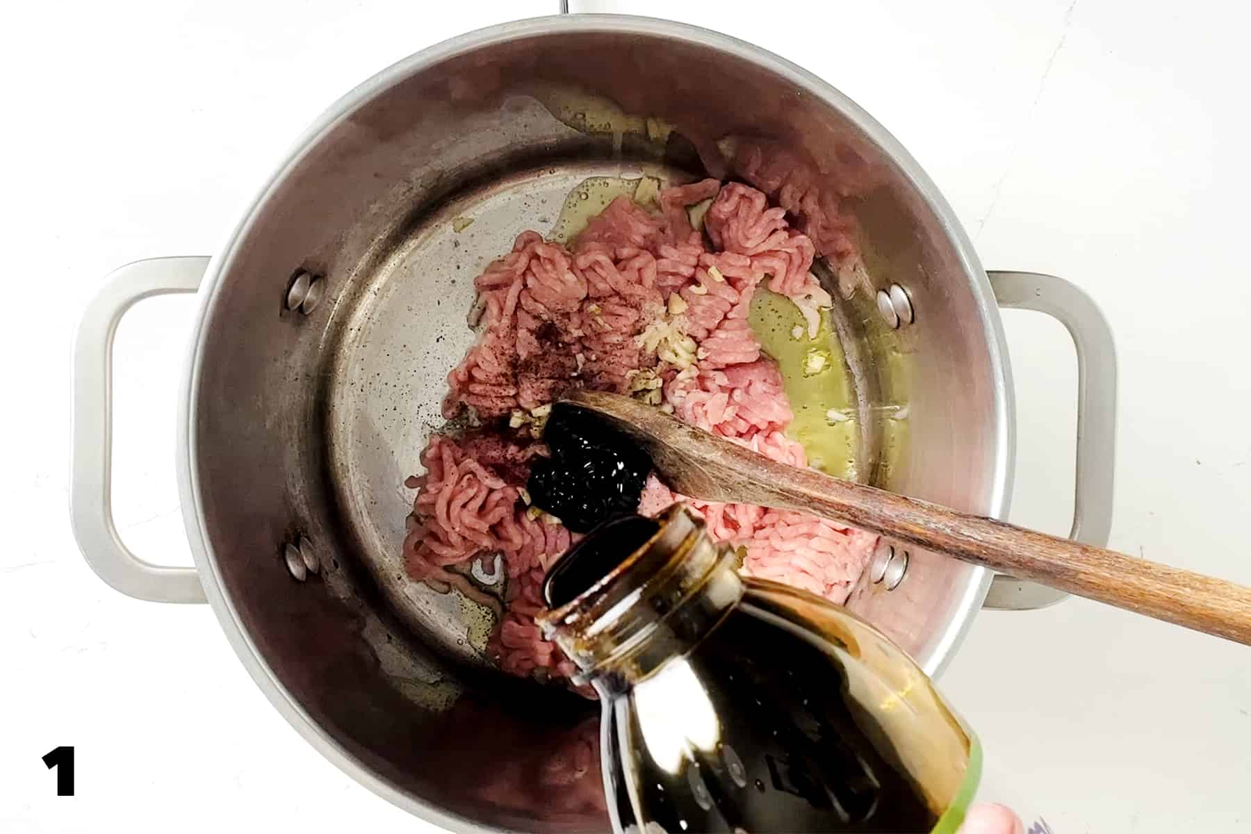 pouring molasses into stock pot with ground pork and wooden spoon